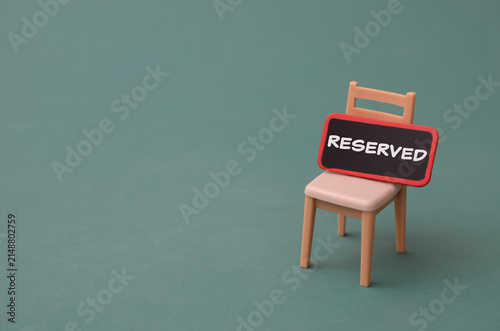 Miniature chair with reserved sign on green background for business booking and vacancy concept