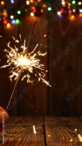 Hand Holding Burning Sparkler Against Blurred Christmas Lights Background