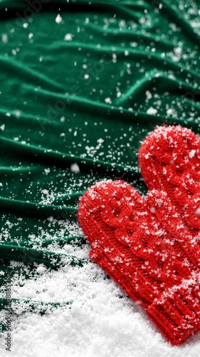 Red Knitted Mittens Resting on Green Velvet Fabric With Falling Snowflakes