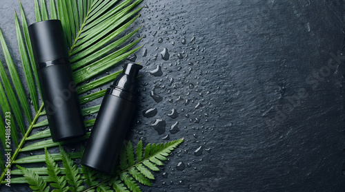 Skincare cosmetic bottles on wet dark stone with tropical leaves skincare cosmetic tropical