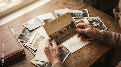 Elderly person hands sorting through vintage black and white historical photographs on wooden table
