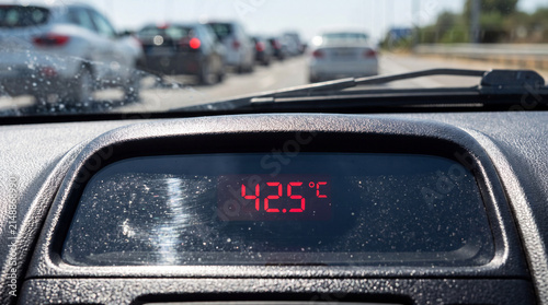 Scorching Temperature on the Road: A car's dashboard displays a blistering 42.5°C, while a line of vehicles stretches into the distance under a clear sky, indicating a sweltering hot day.