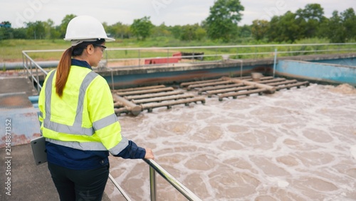 Canvas Print Asian woman worker checking industrial water treatment facility and wastewater basin with laptop and clipboard