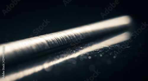 Polished Metal Rod Resting on Dark Reflective Surface with Dramatic Macro Lighting for Industrial Design Concept