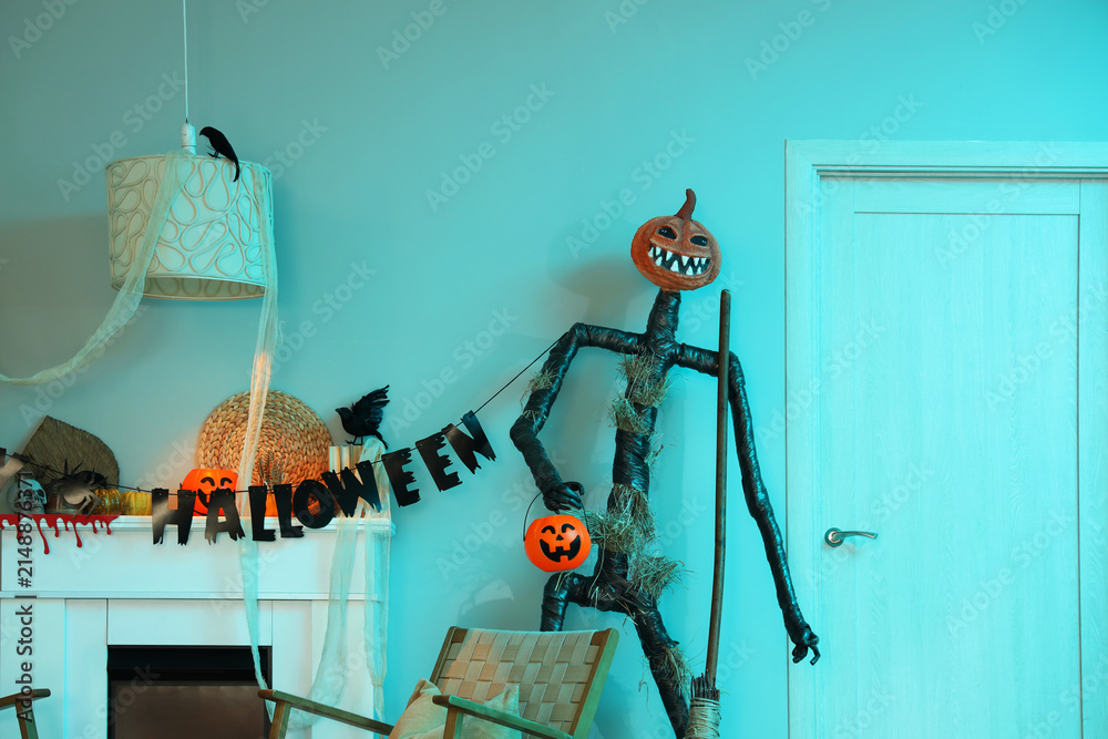 Obraz premium Interior of festive living room with armchair, garland, Spooky Halloween monster and autumn decorations on fireplace