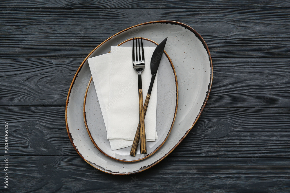 Obraz premium Plates with cutlery and paper napkins on black wooden background
