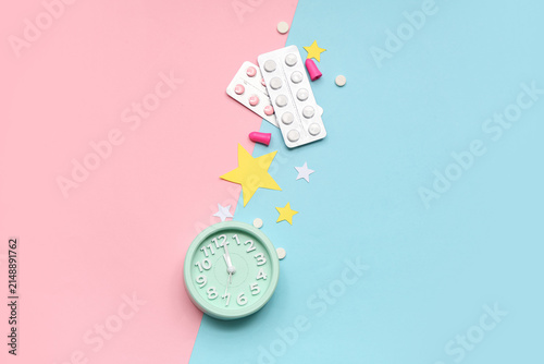 Cuadro en lienzo Alarm clock with sleeping pills, paper stars and earplugs on color background