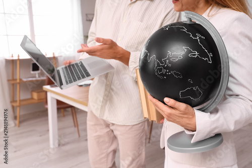 Teachers with globe using laptop in school office, closeup