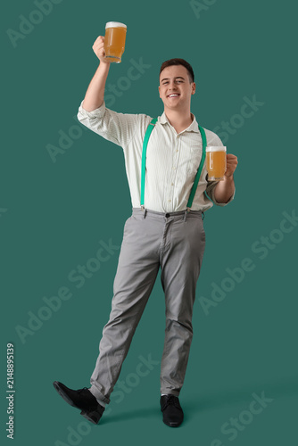 Handsome young happy man in traditional German clothes with mugs of beer on g...
