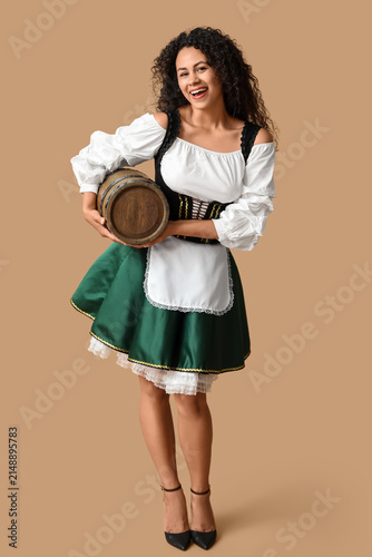 Happy African-American woman with barrel of beer on beige background. October...