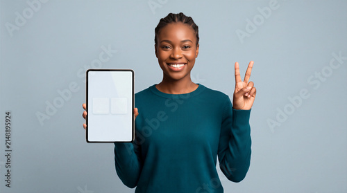 Smiling businesswoman showing a blank tablet mockup and peace sign against a studio background