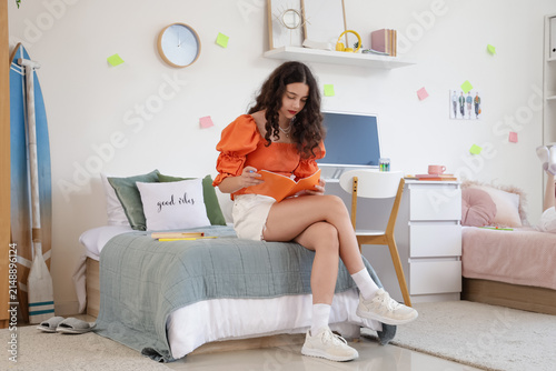 Female student with copybook studying in dorm room