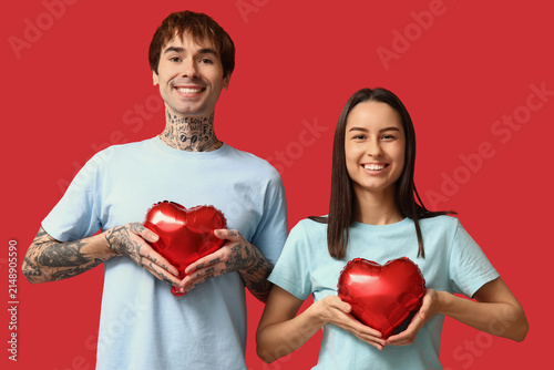 Young couple with heart-shaped air balloons on red background
