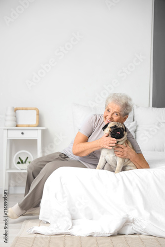 Senior woman with pug dog in bedroom