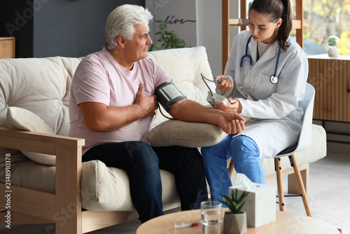 Young nurse measuring blood pressure of senior man at home