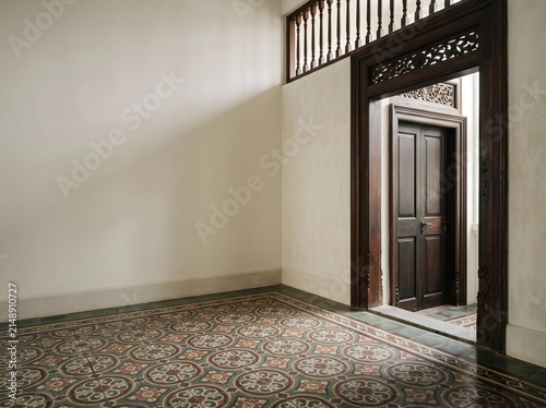 Empty room corner with Peranakan tile floor and carved wood door