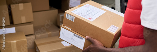 Cropped shot of courier holding cardboard boxes with shipping labels near delivery van. Image represents logistics and e-commerce supply chain services, close up