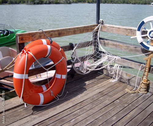 Foto Wooden pier corner with an orange lifebuoy, a draped fishing net adorned with a skull, and a decorative ship's wheel