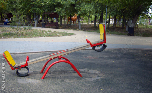 Fotografía A vibrant red and yellow seesaw sits on a dark playground surface