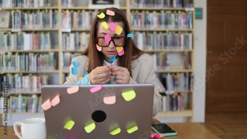 Overworked office employee sorts sticky note reminders while facing an endless task list at her laptop showing mental overload from excessive workload and tight deadlines
