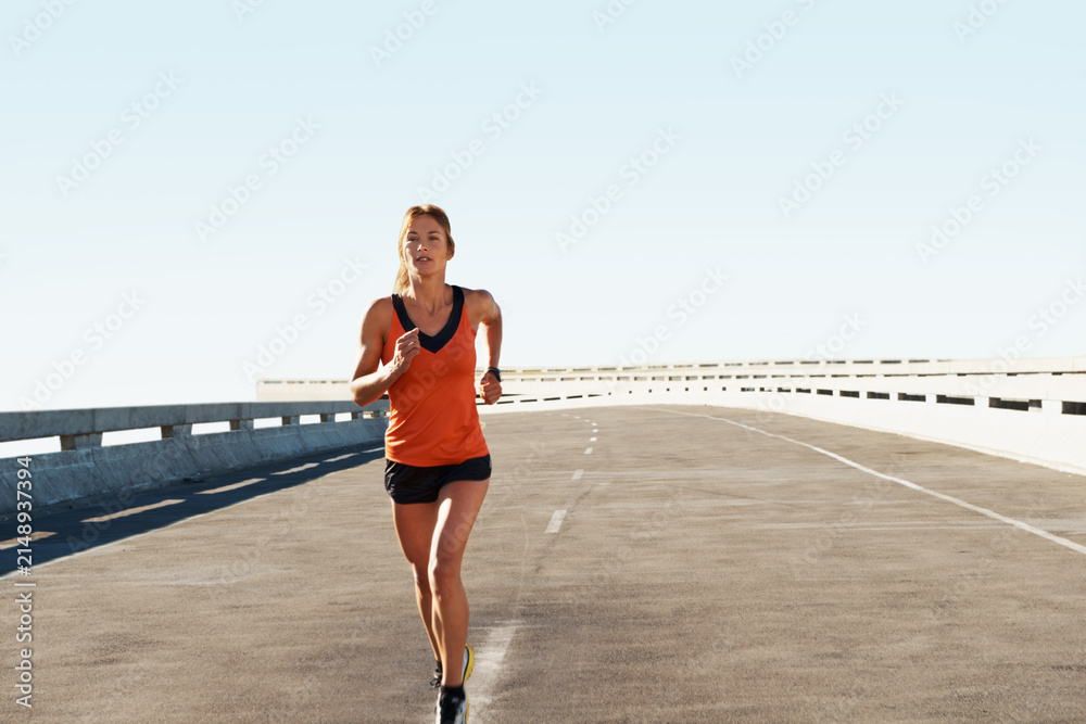 Obraz premium Workout, woman and running for fitness in road with pace training, morning cardio and practice. Space, serious athlete and jog on highway bridge for exercise routine, endurance or health and wellness