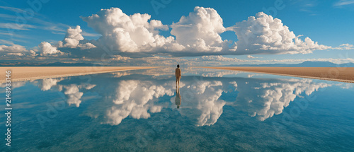 Lone man standing on mirror-like salt flat reflecting blue sky and massive clouds 