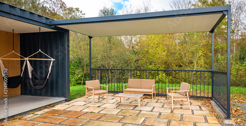 Outdoor living space built from recycled shipping containers featuring a modern pergola covering patio furniture and lounge area with hammocks, offering relaxation and design surrounded by nature