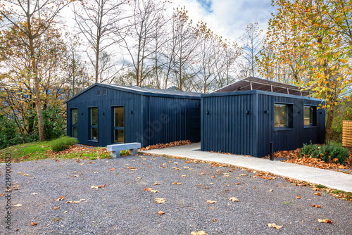 Modern office building constructed from shipping containers, featuring solar panels, blending contemporary sustainable architecture with the surrounding autumn nature of forest