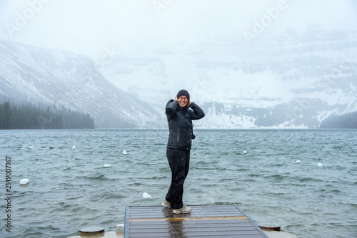 Happy woman stands on a pier in Cameron lake during winter weather