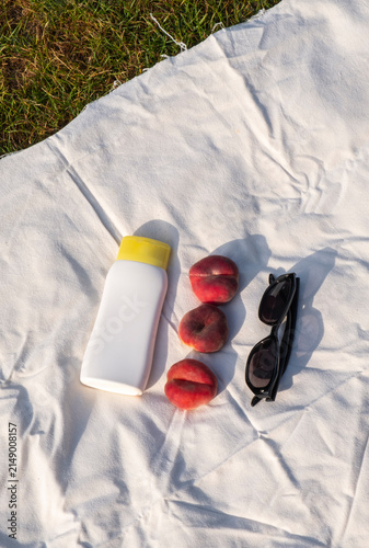 Fresh ripe peaches, sunglasses and sunscreen on a blanket outdoors, capturing a peaceful summer lifestyle.