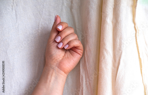 Close-up of female hands with pastel nail polish against a neutral beige textile background.