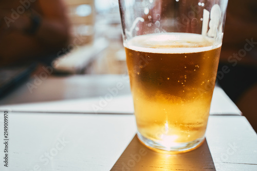 Photography Close-up of a refreshing pint glass filled with golden craft beer on a table