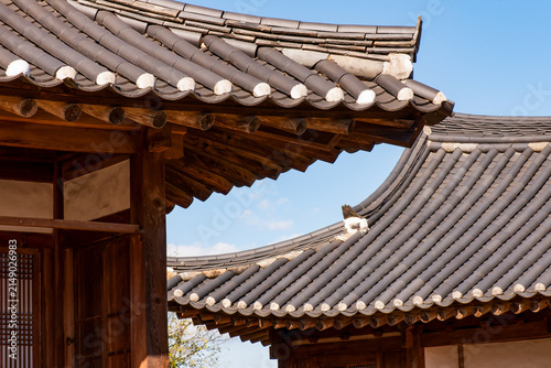Traditional Korean hanok vernacular architecture horizontal composition featuring curved tiled roofs and wooden eaves against blue sky