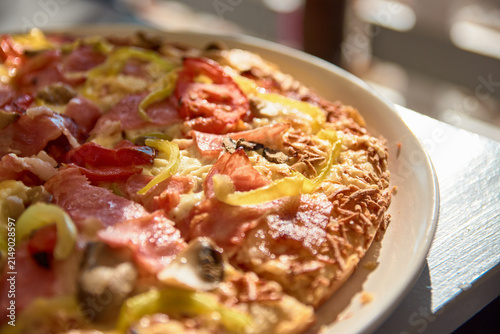 Close-up of freshly baked delicious pizza with melted cheese and ham on a white plate