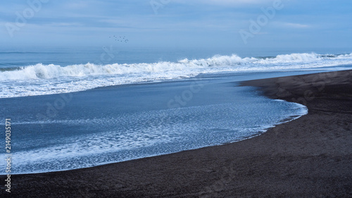 Foto Foamy tide curving across a black sand beach on the Hokkaido Pacific coast