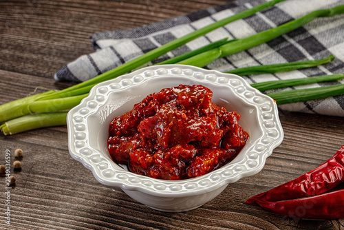 Foto Spicy red chili sauce in white ceramic bowl with green onions and dried chilies