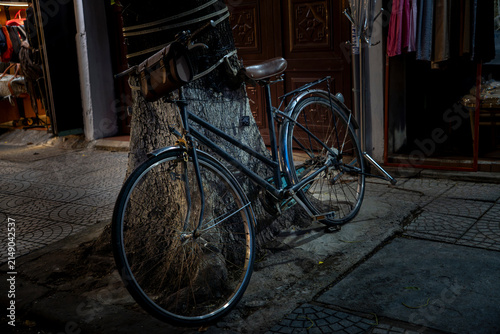 Konstfotografi Vintage bicycle with leather bag leaning against a tree on a cobblestone street