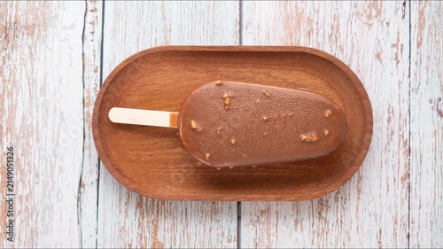Timelapse: dissolution of popsicle ice cream on wooden plate. Top view, wooden background	