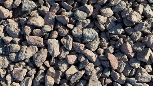 Closeup small gravel stones texture, sunlit rough pebbles in muted brown and gray tones, scattered angular fragments forming dense