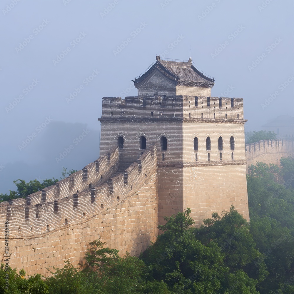Naklejka premium A majestic segment of the Great Wall is shrouded in morning mist, surrounded by lush greenery, This serene image is ideal for travel, history, or cultural themes in various media,
