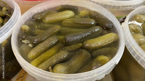Fresh market pickles in container, closeup of clear plastic tub packed with brined cucumbers, glistening brine