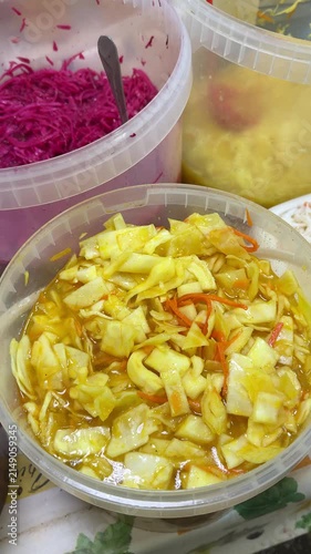 Close-up sauerkraut with turmeric saffron, glossy yellow cabbage shreds in plastic bucket at bustling vegetable market, carrot