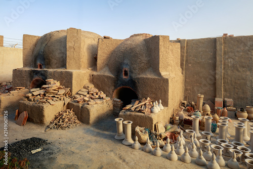 View of traditional mud-brick kilns used for firing pottery, surrounded by numerous unglazed clay vessels and ceramic objects in a workshop setting in Hala, Sindh, Pakistan.