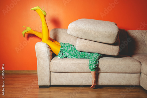 Woman in green dress and yellow tights humorously buried under sofa cushions