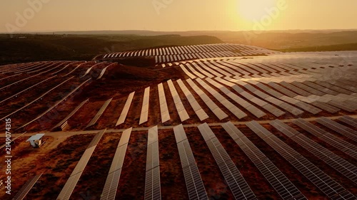 Aerial view of expansive photovoltaic arrays arranged across rolling countryside in warm evening light. 