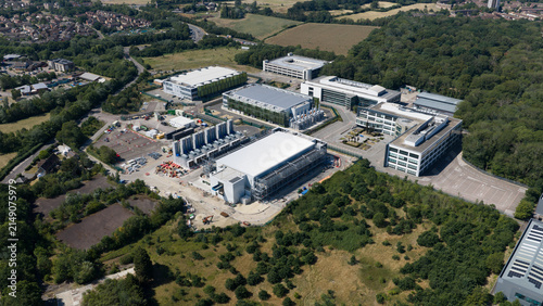Aerial view of the Kao Data campus featuring modern industrial buildings, data center facilities, surrounding woodland, and parking areas in Harlow, England, United Kingdom.