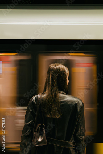 Young woman standing on an underground subway platform from behind while a fast train passes by with dynamic motion blur. Warsaw metro