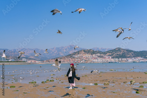 Foto Woman watching seagulls take flight on coastal tidal flat, Shazikou, Qingdao