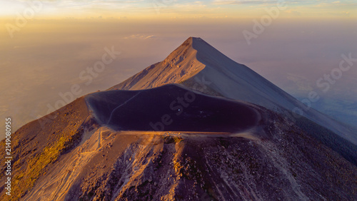 Aerial view of Acatenango volcano crater at sunset with golden light illuminating the volcanic slopes and rocky terrain in Alotenango, Sacatepequez Department, Guatemala.