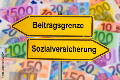Zwei Wegweiser über vielen Euro Banknoten zeigen in unterschiedliche Richtungen mit der Aufschrift Beitragsgrenze und Sozialversicherung  - FOTOMONTAGE